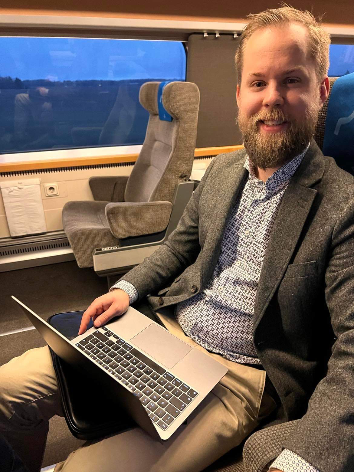Foto av Markus som sitter på ett tåg, iklädd kavaj, och ser in i kameran.